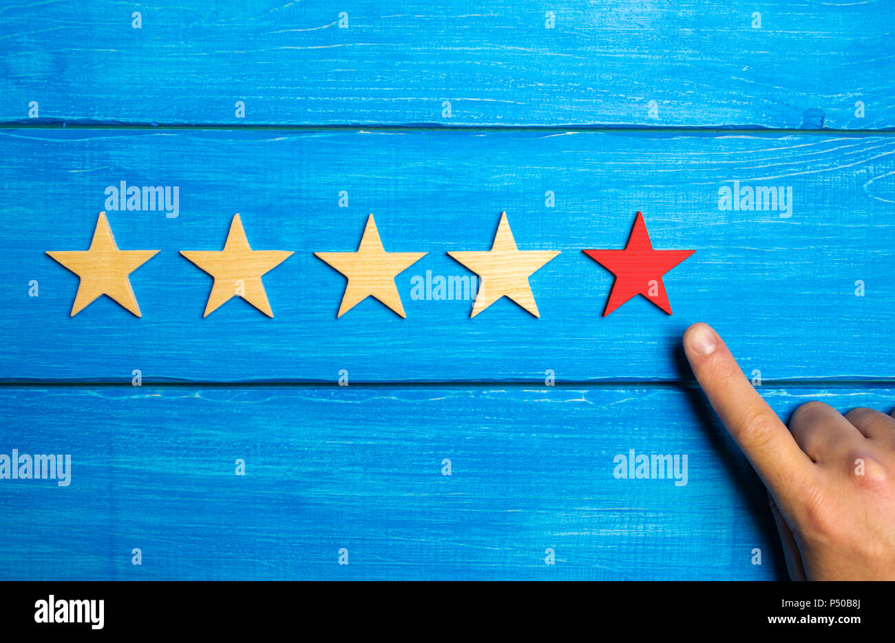 The male hand points to the fifth red star on a blue wooden background. Five Stars. Rating of restaurant or hotel, application. Evaluation of quality  Stock Photo