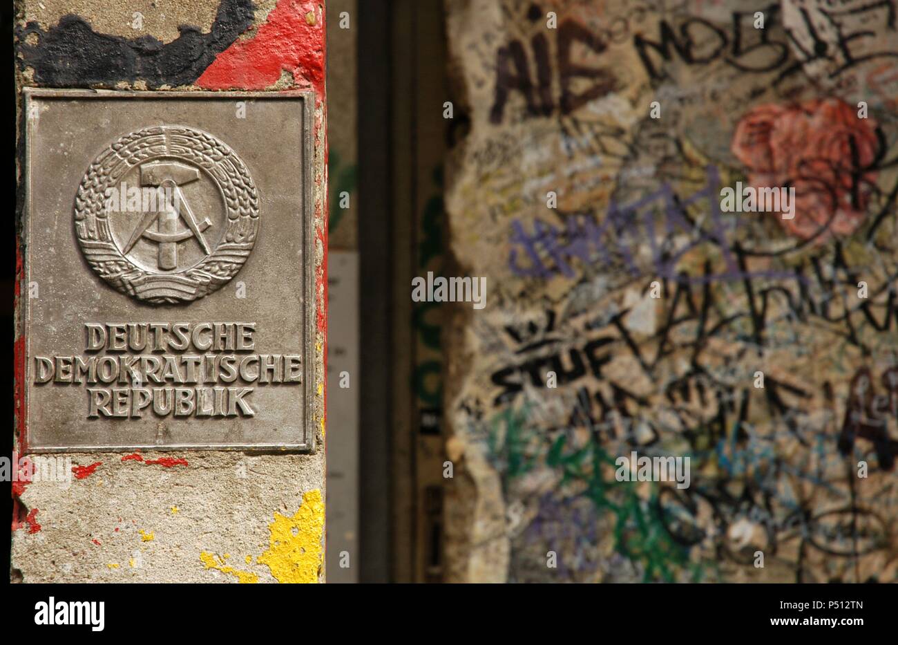 Germany. Berlin. The National Emblem of the German Democratic Republic. A hammer and a compass, surrounded by a ring of rye next to a section of the Berlin Wall. Stock Photo