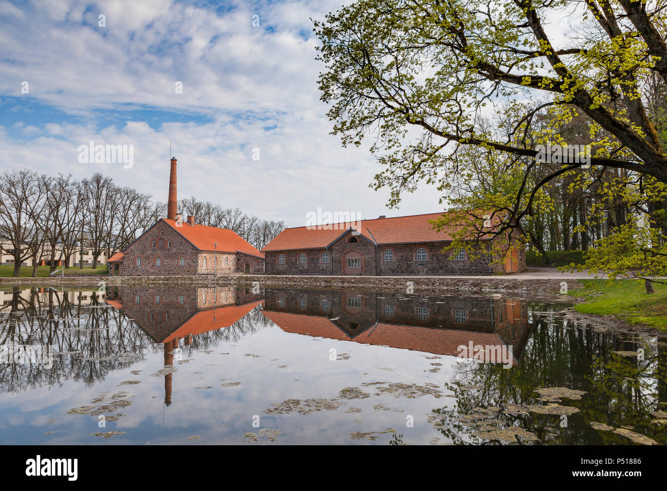 Old Olustvere manor park in the summer time. The manor's vodka distillery buildings are reflected in the park's pond. located in the middle of Estonia Stock Photo