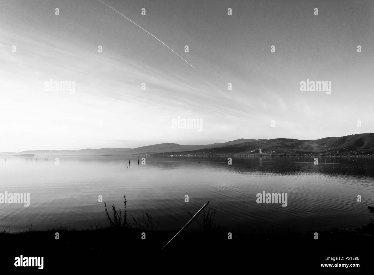 Beautiful view of Trasimeno lake (Umbria, Italy), with hills and sky reflecting on water and a wooden pole on the shore in the foreground Stock Photo