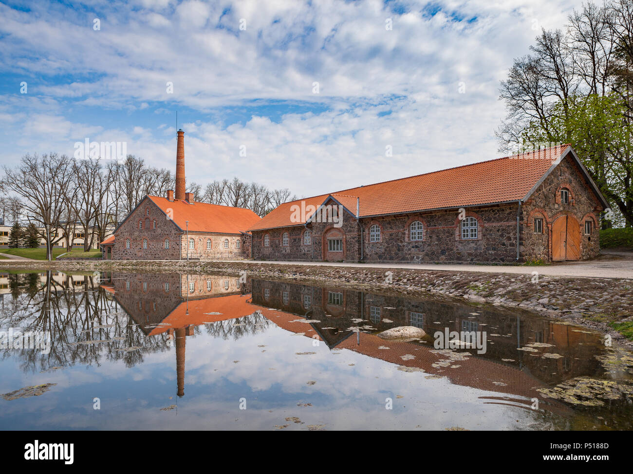 Old Olustvere manor park in the summer time. The manor's vodka distillery buildings are reflected in the park's pond. located in the middle of Estonia Stock Photo