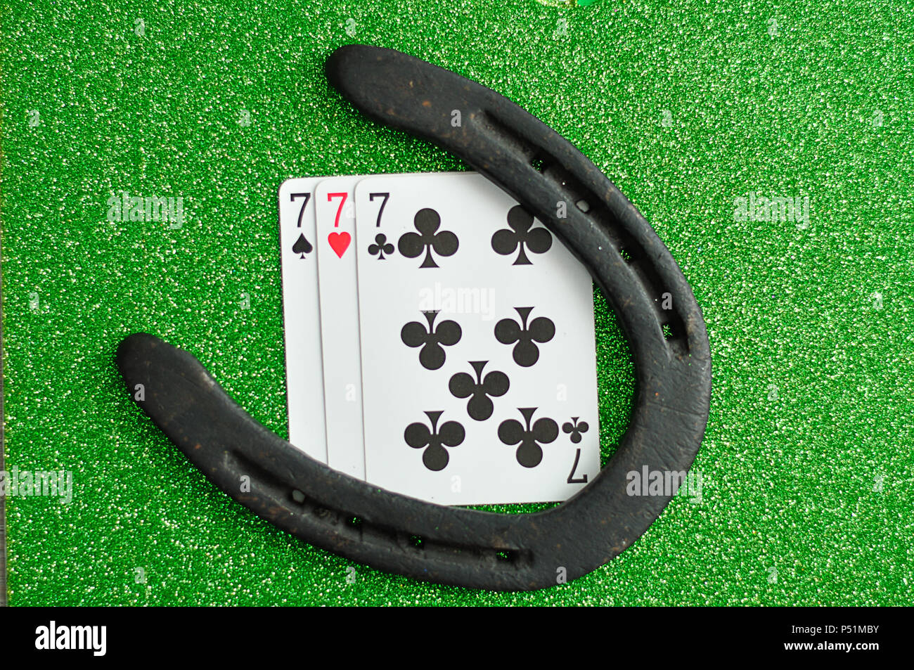 A horseshoe and three number seven cards on a green background Stock ...