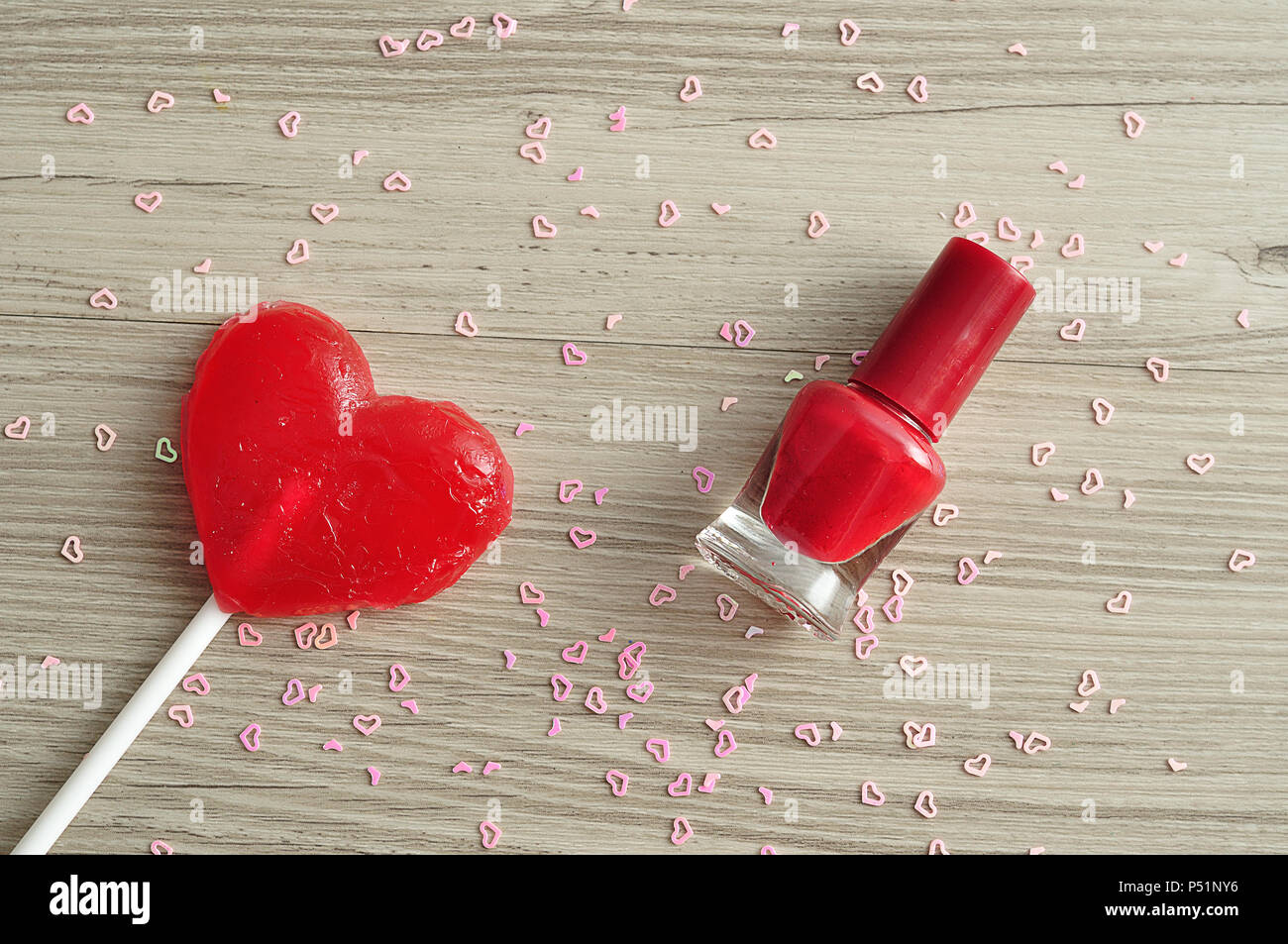Red nail polish displayed with a red heart shape lollipop and pink heart nail art on a wooden background Stock Photo