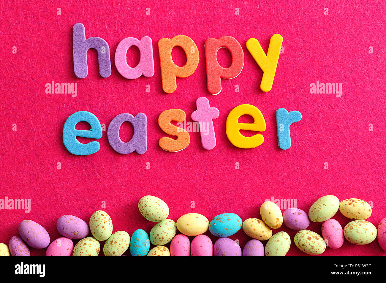 The words happy easter displayed with speckled easter candy eggs on a pink background Stock Photo