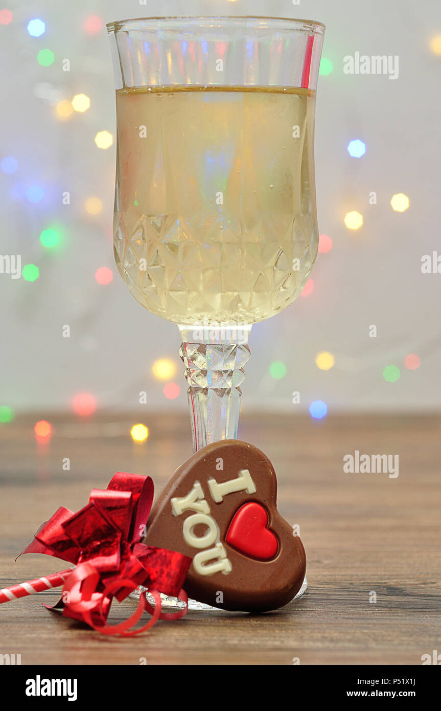 A heart shape chocolate lollipop with the words I love you and a glass of champagne against an out of focus light background Stock Photo