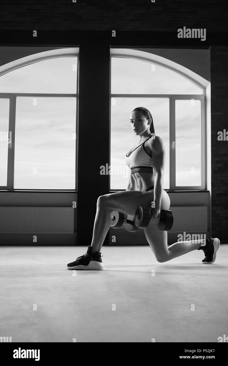 Black and white photo of strong woman doing fitness exercises with dumbbells. Looking healthy, strong, fit, feeling good. Going to gym. Having athletic muscles and stunning figure, body. Stock Photo