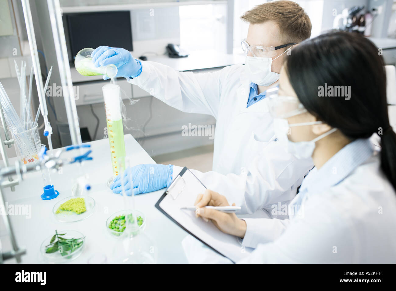 Microbiologists conducting experiment with green vegetable sample Stock Photo