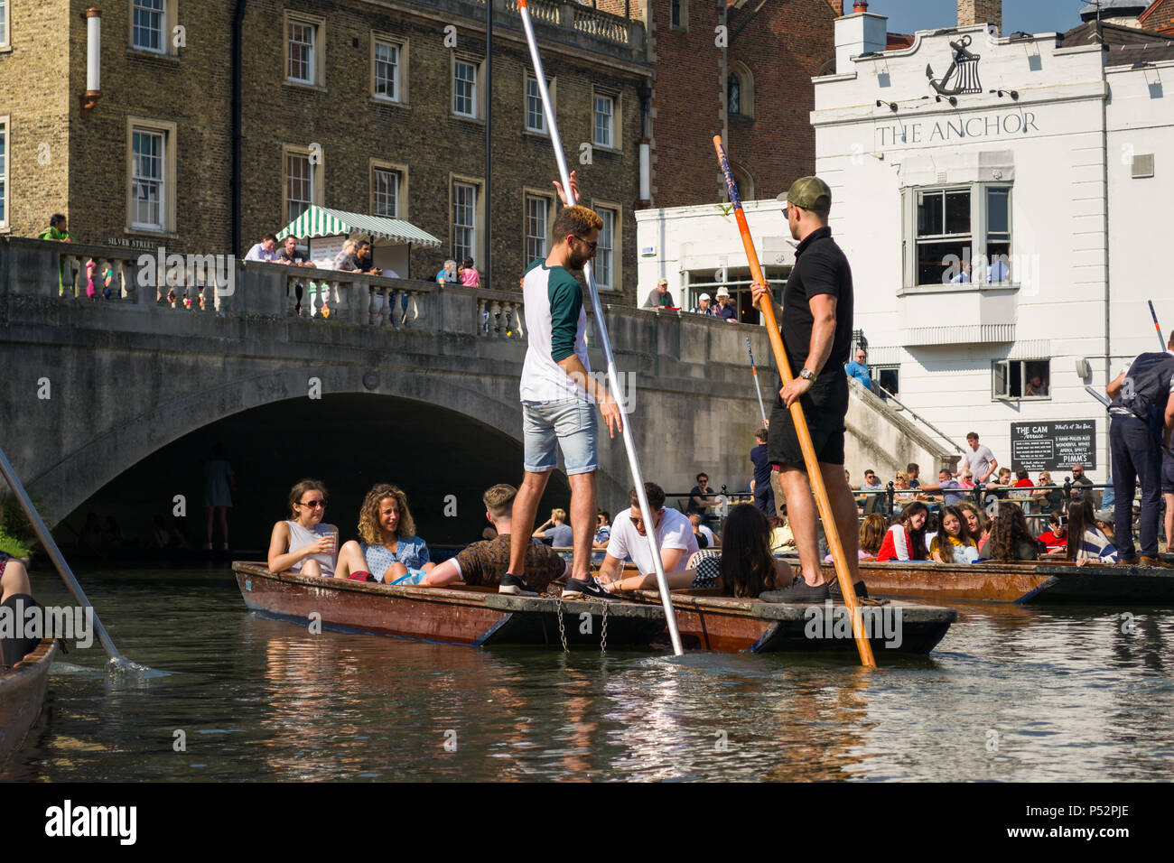 People on punt boats punting on the river Cam as people walk alongside it on a sunny Summer afternoon, Cambridge, UK Stock Photo