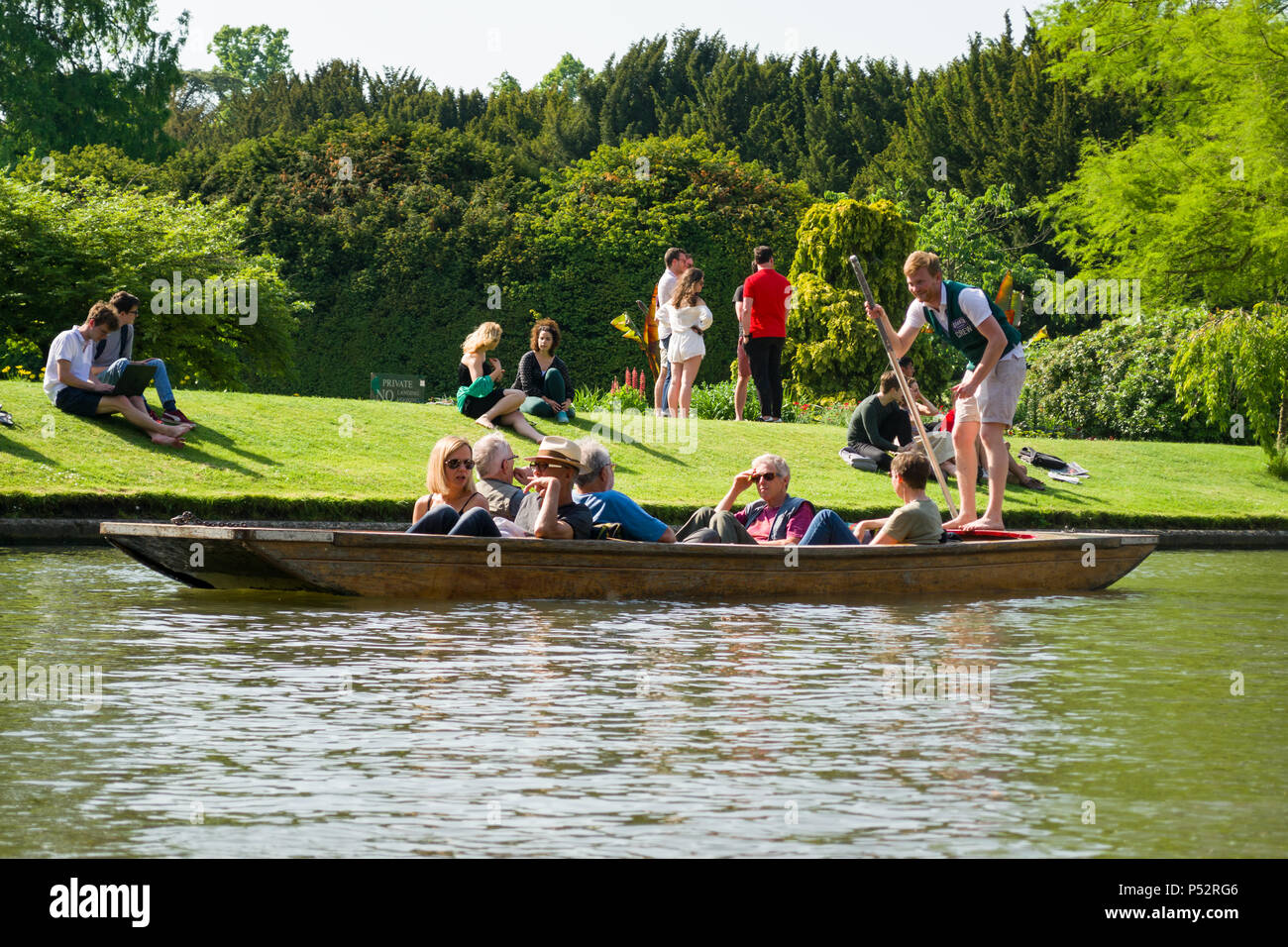 People on punt boat punting on the river Cam as people sit alongside it on a sunny Summer afternoon, Cambridge, UK Stock Photo