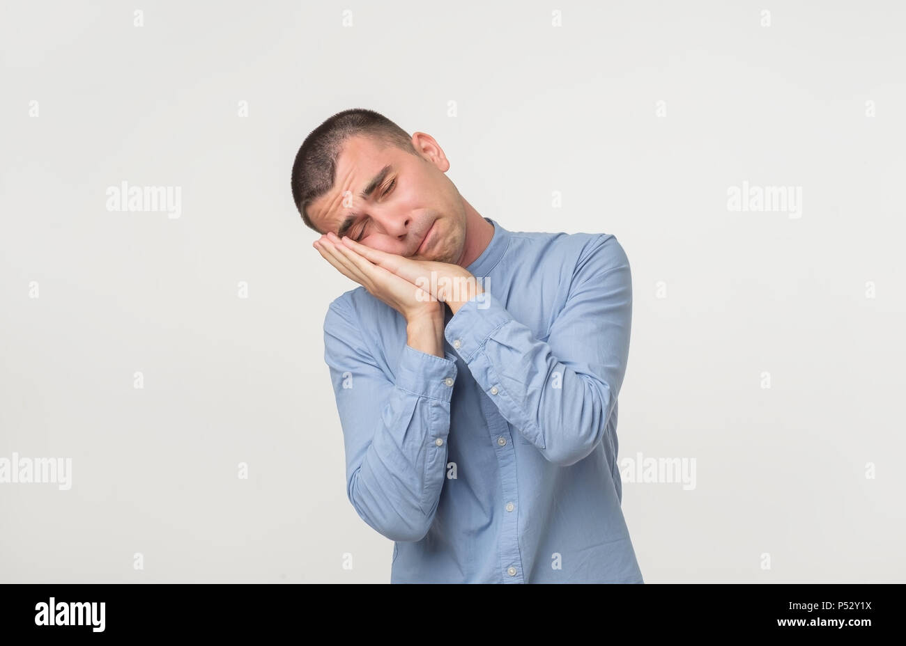 Young man wearing a blue shirt outfit putting his palms like a pillow. Looking sleepy and tired. No energy concept Stock Photo