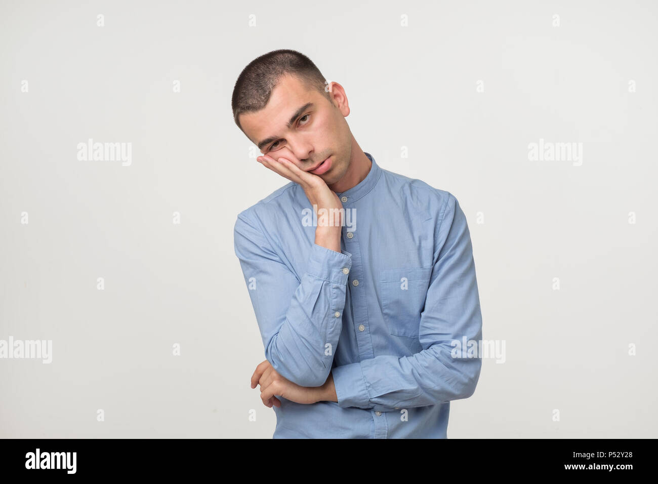 Young man wearing a blue shirt outfit putting his palms like a pillow. Looking sleepy and tired. No energy concept Stock Photo