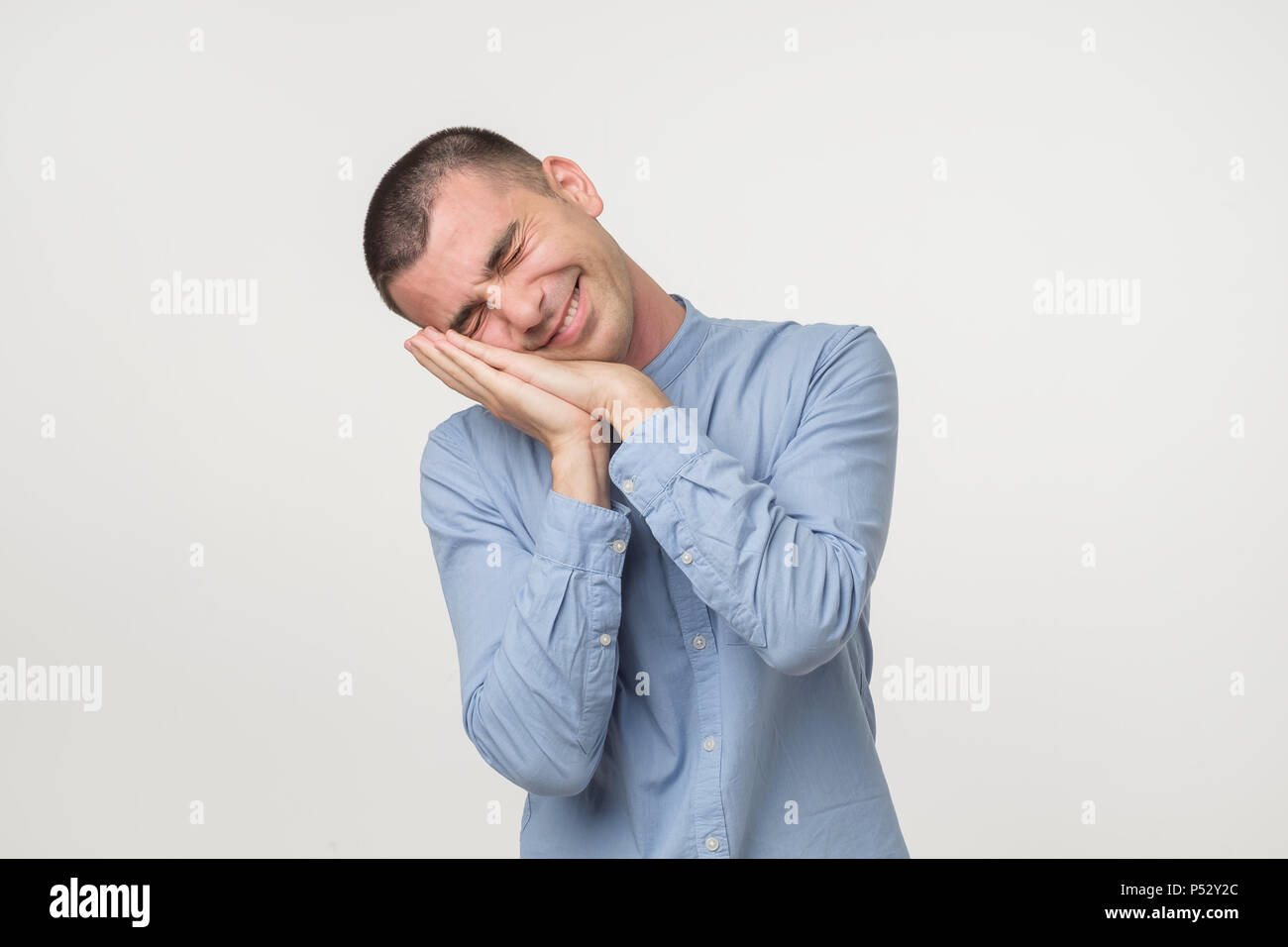 Young man wearing a blue shirt outfit putting his palms like a pillow. Looking sleepy and tired. No energy concept Stock Photo