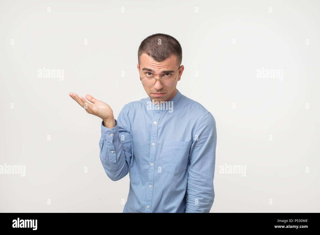 Young man in blue shirt standing disorientated bewildered isolated on gray wall background. Decision making concept. Human facial expression emotions Stock Photo