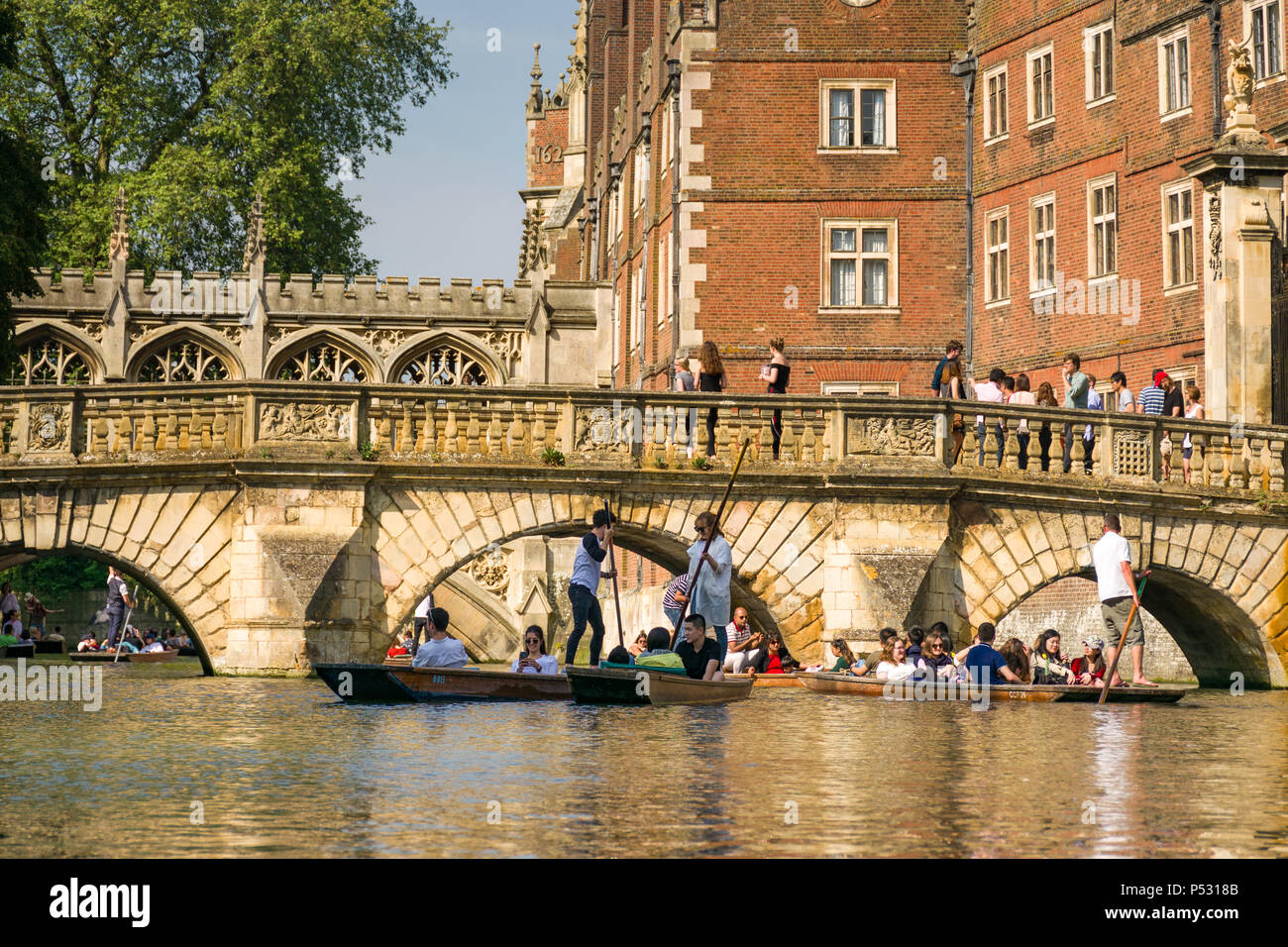 People on punt boats punting on the river Cam as people walk along a bridge by St Johns college university on a sunny Summer afternoon, Cambridge, UK Stock Photo