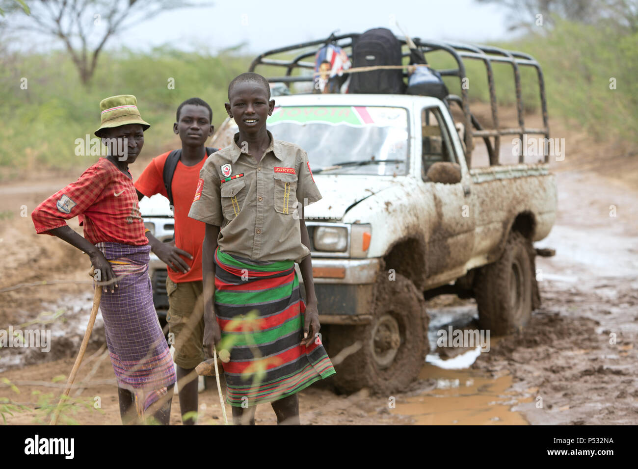 KAKUMA, KENYA - Three boys are standing in front of a pickup truck on a country road outside the Kakuma refugee camp. Stock Photo