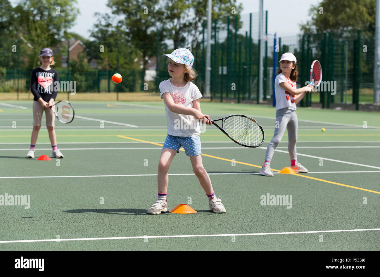 Children's tennis coaching session / lesson taking place on a full-size tennis court with kids / kids and professional tennis coach, in summer. UK. (99) Stock Photo