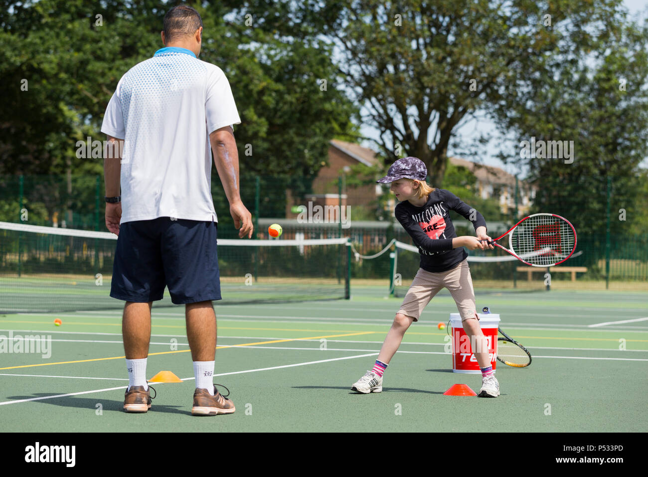 Children's tennis coaching session / lesson taking place on a full-size tennis court with kids / kids and professional tennis coach, in summer. UK. (99) Stock Photo