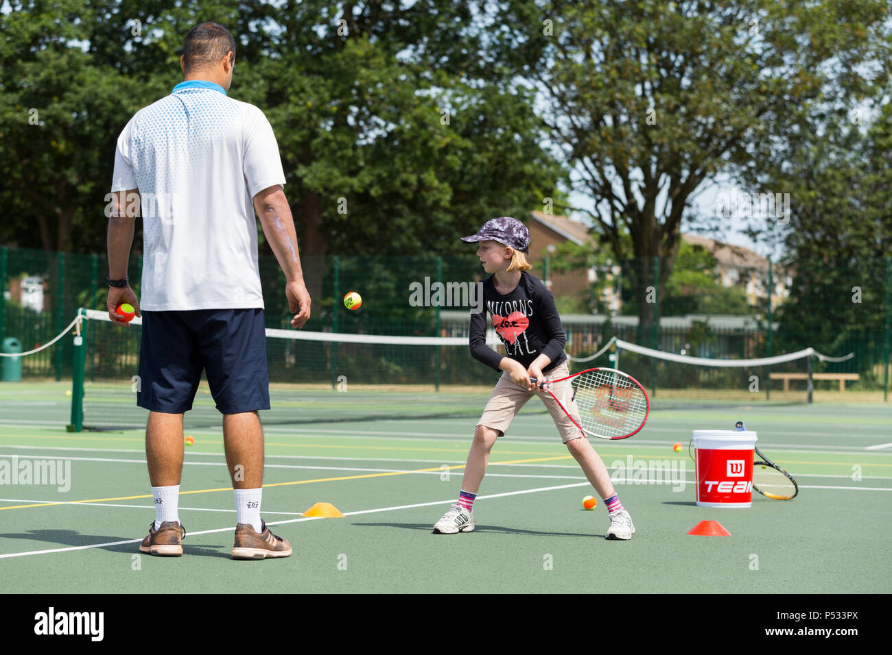 Children's tennis coaching session / lesson taking place on a full-size tennis court with kids / kids and professional tennis coach, in summer. UK. (99) Stock Photo