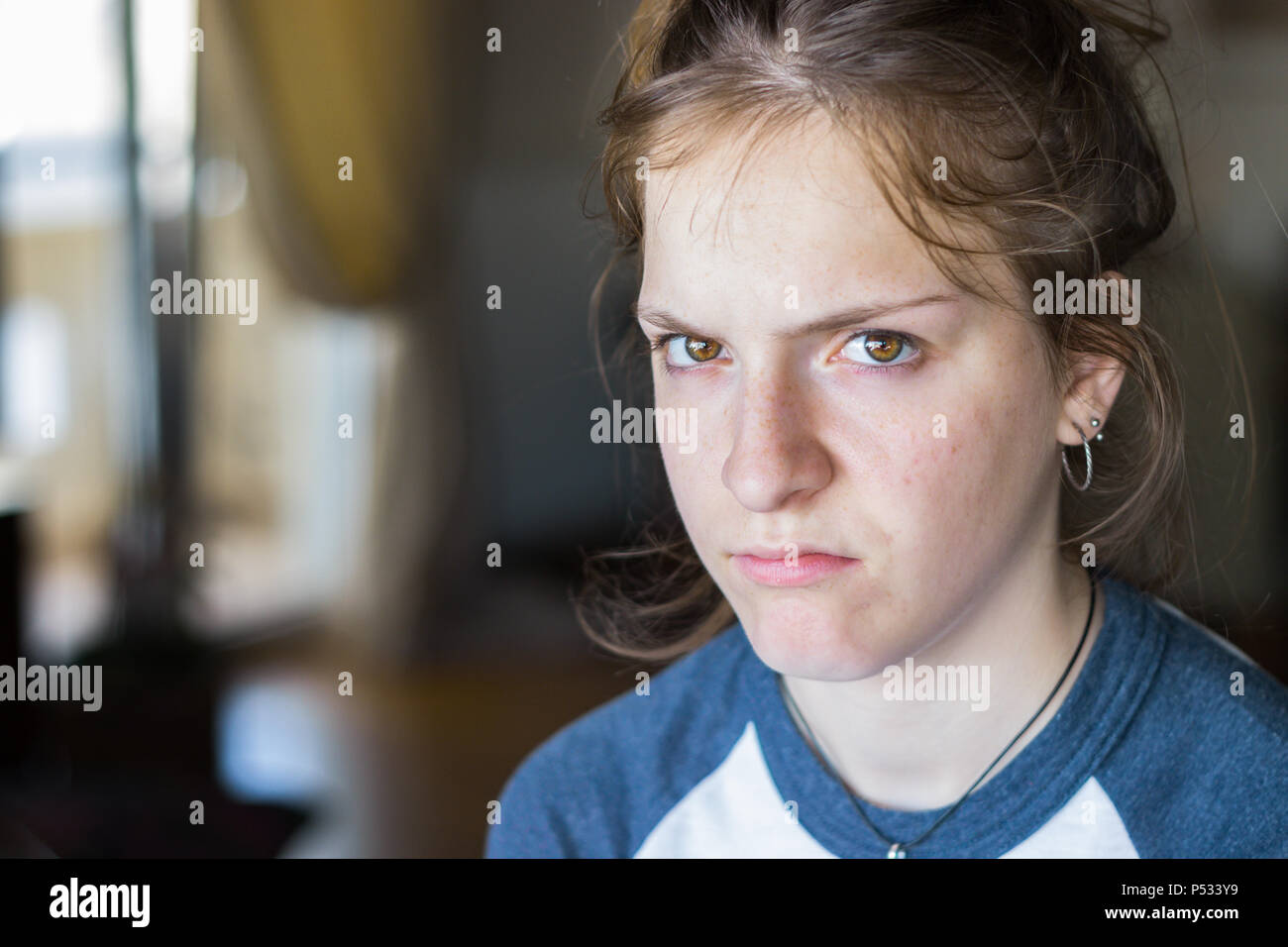Portrait of a young girl with an anger and upset face looking camera, indoors. Stock Photo