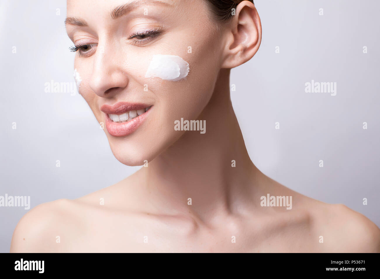 Laughing girl applying moisturizing cream on her face. Photo of young girl with flawless skin on grey background. Skin care and beauty concept Stock Photo