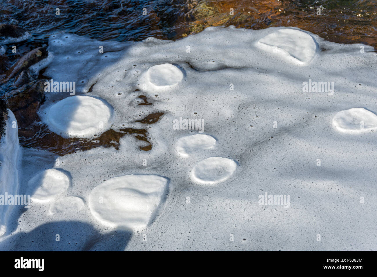 Frozen foam pancakes eroded into circles by being rotated while circulating in an eddy in the river Coupall, Glencoe, Highland Region, Scotland, UK Stock Photo
