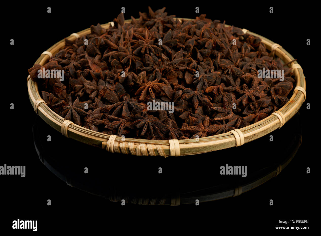 Star anise spice on wicker plate isolated on black reflective background Stock Photo