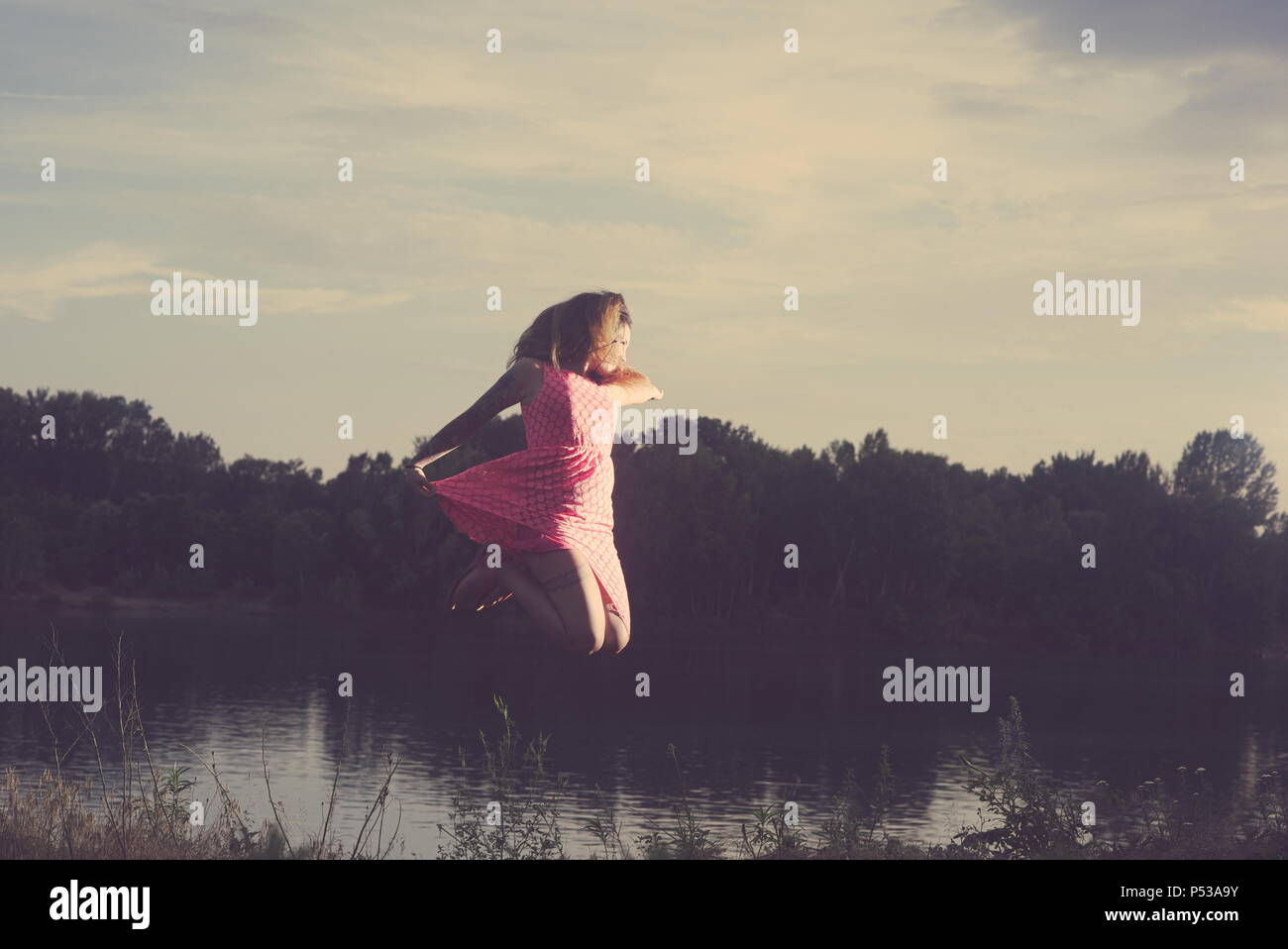 Young Tattooed Woman Jumping over the Lake on a Summer Day Stock Photo
