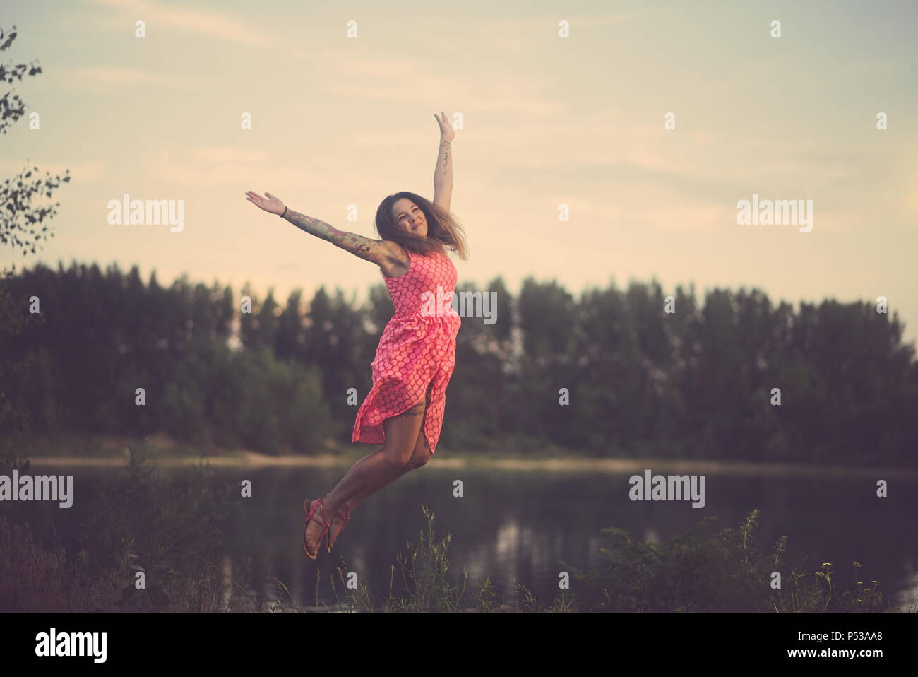 Young Tattooed Woman Jumping over the Lake on a Summer Day Stock Photo