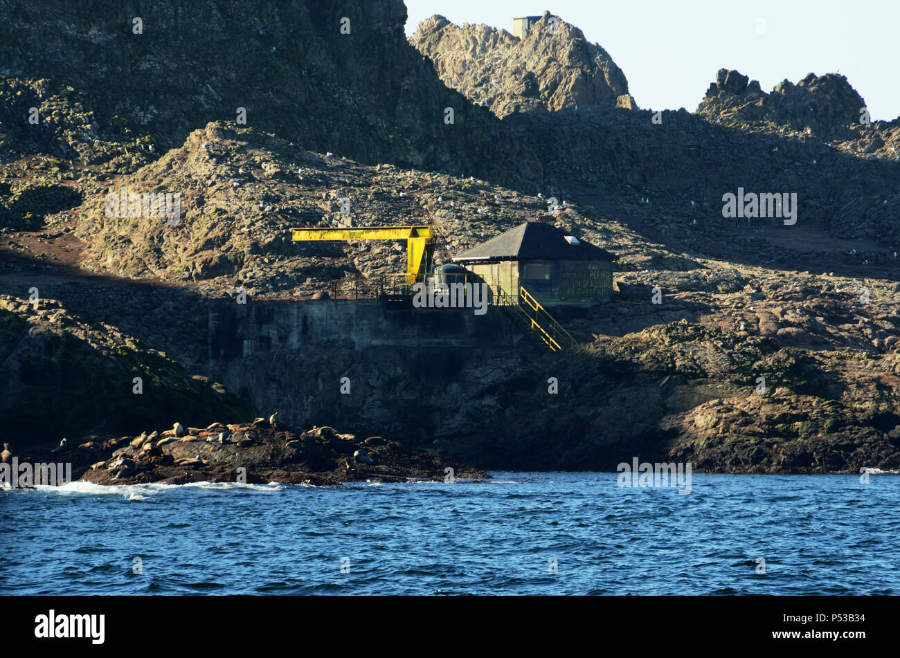 A building with 'Federal Wildlife Refuge No Trespassing No Shooting' painted on the side of it and an old crane on the Southeast Farallon Island Stock Photo