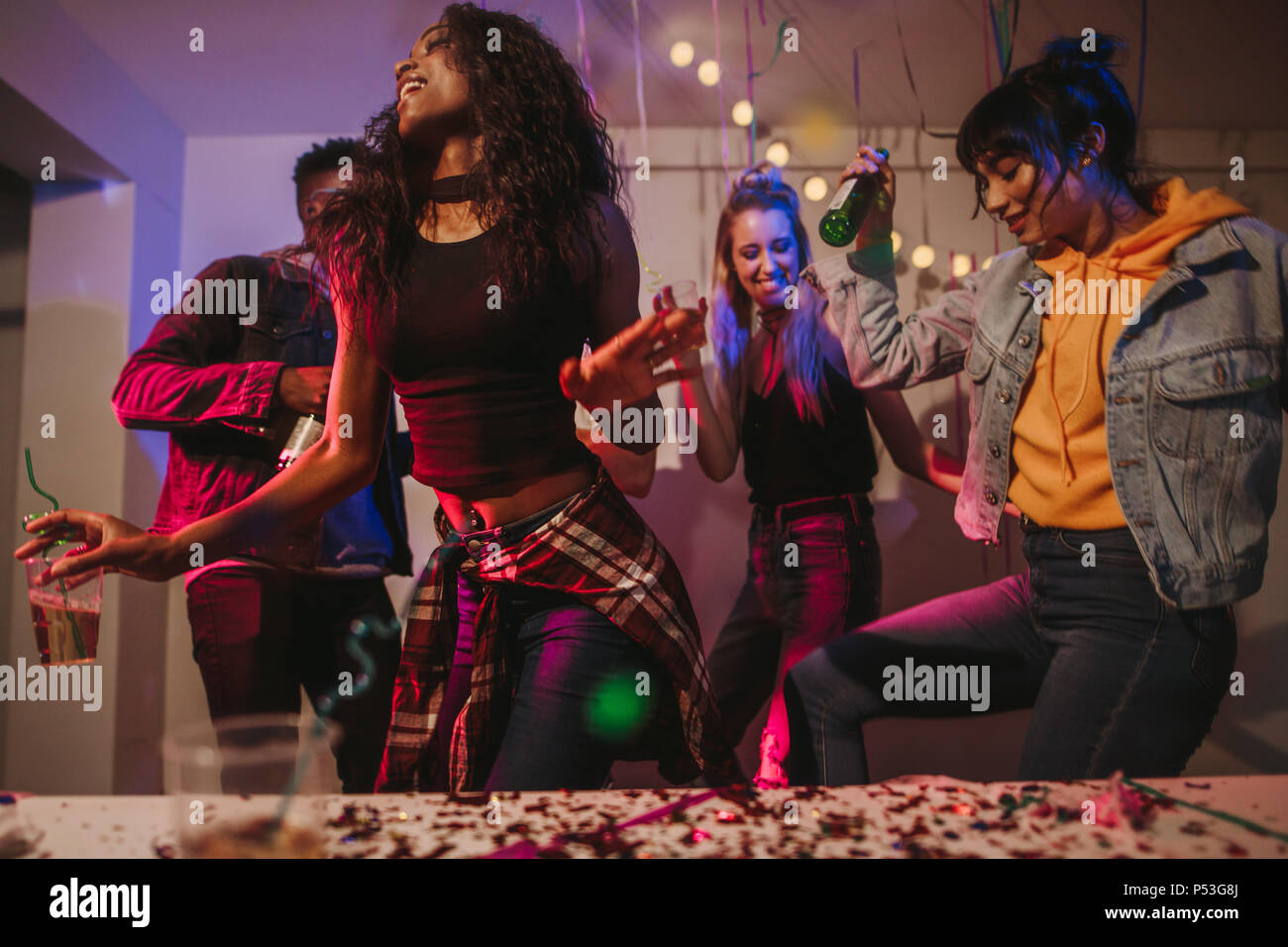Friends dancing holding drinks at house party. Young women enjoying and having fun at the house party. Stock Photo