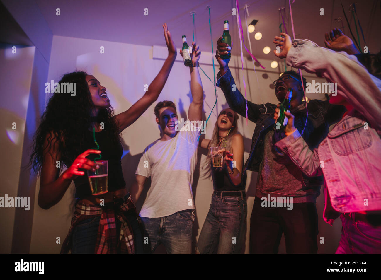 Friends toasting drinks at a house party. Young men and women having fun at a colorful house party with confetti all around. Stock Photo