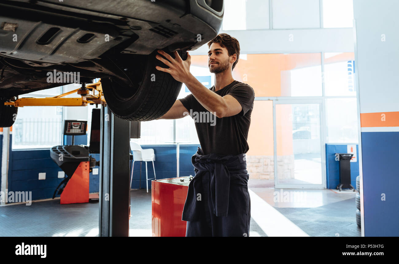 Auto mechanic replacing a wheel of car in service station. Young male fixing wheel on a lifted vehicle in auto repair shop. Stock Photo