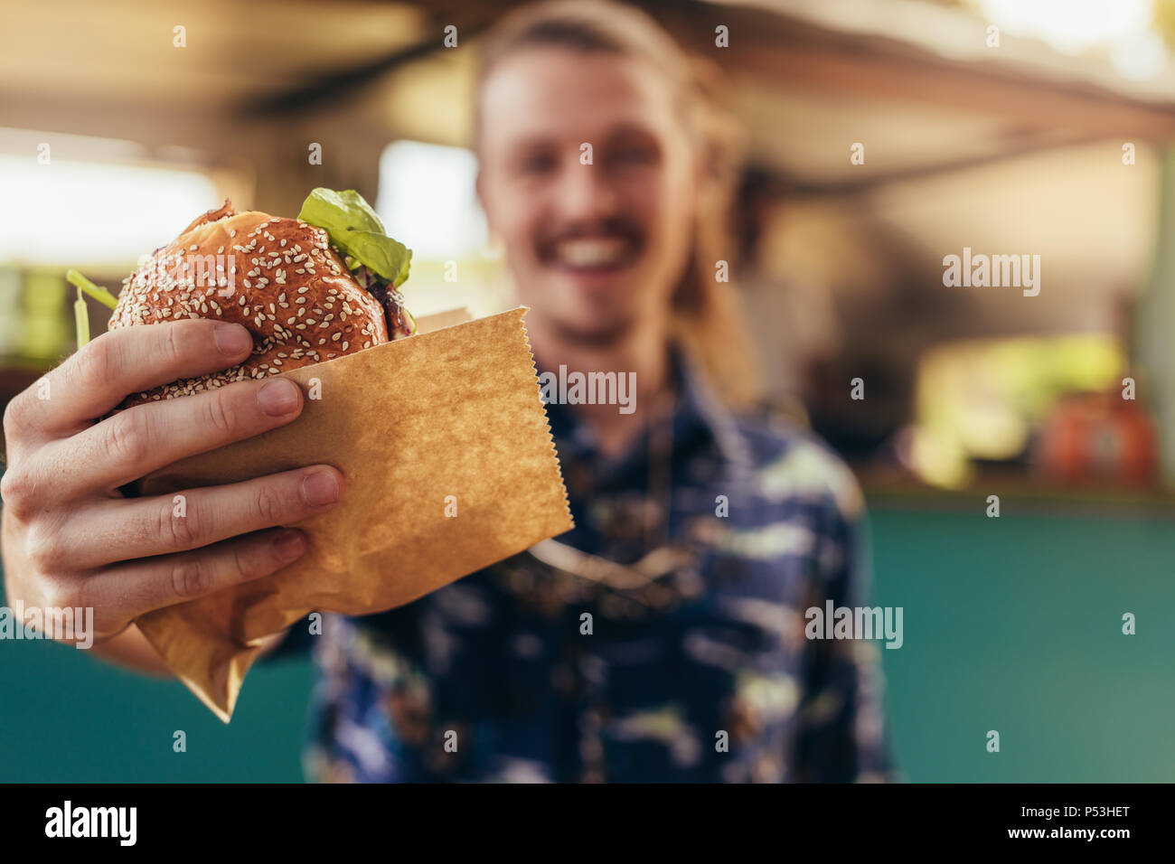 Closeup of young hipster man holding a burger in hands. Focus on hands holding food truck burger. Stock Photo
