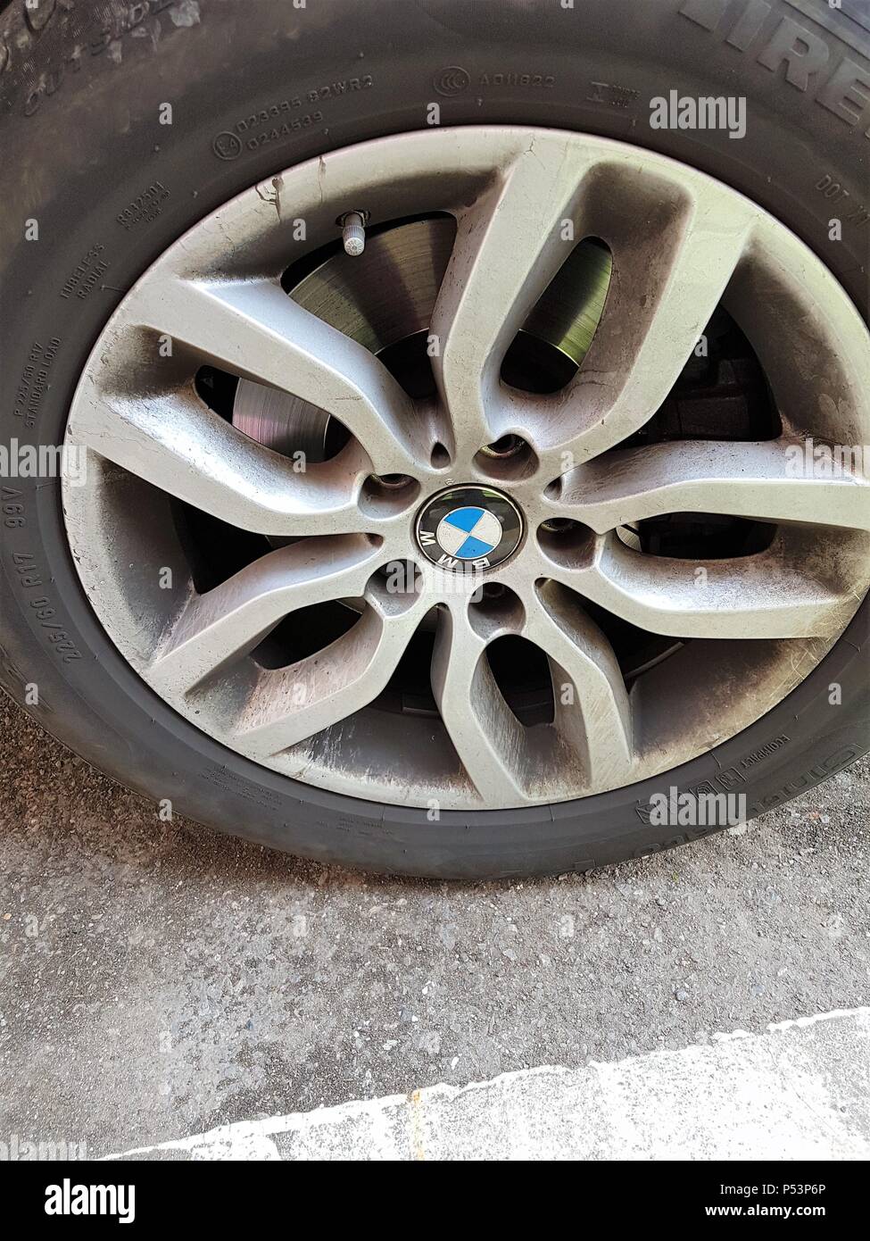 Parked car with a Firelli car tyre with a BMW wheel cap next to a white painted line on road Stock Photo