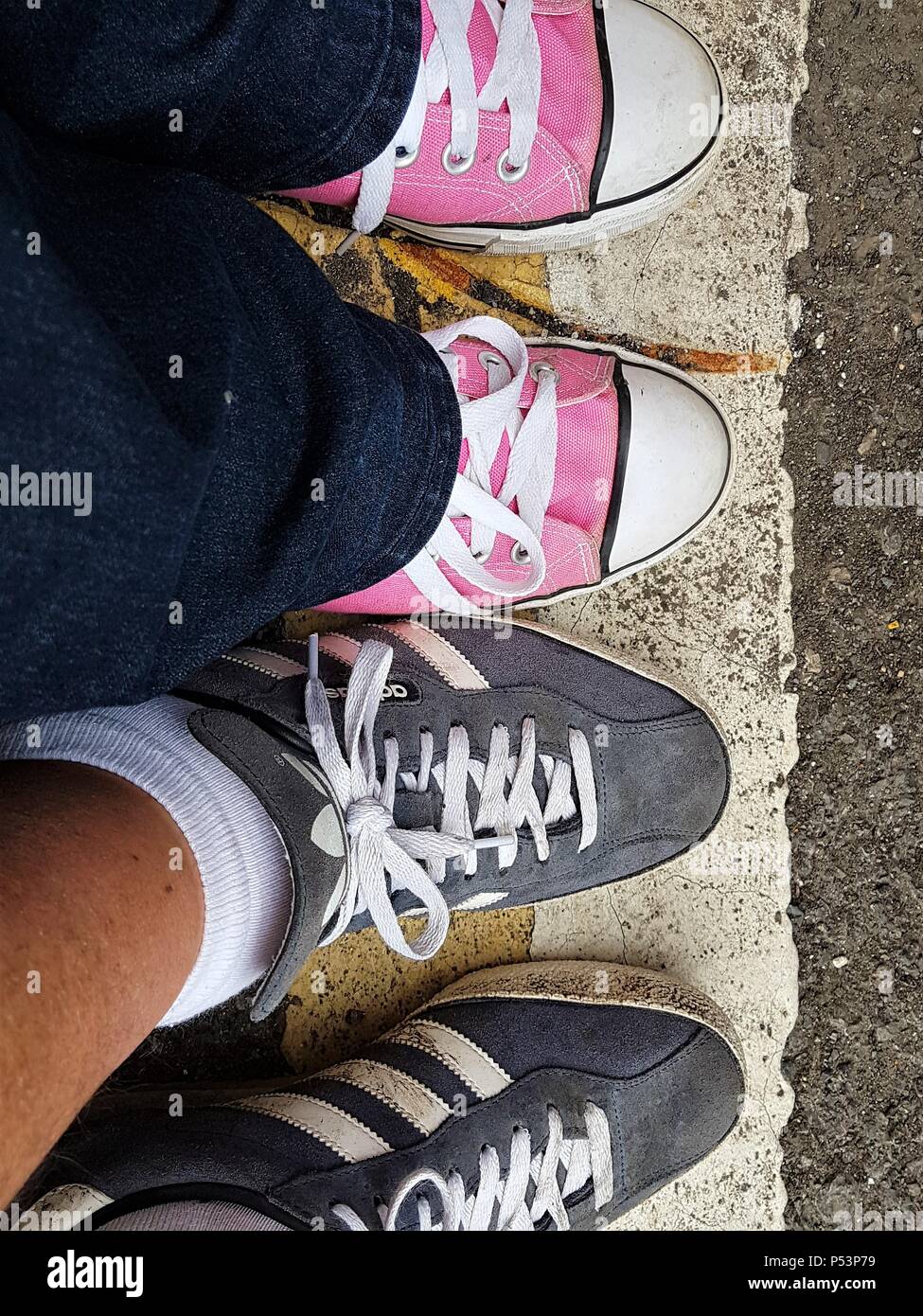 Downward view of 2 people wearing pink and blue trainers standing on white and yellow lines on a road. Stock Photo