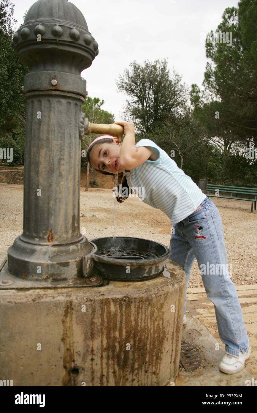 Niña de siete años bebiendo agua en una fuente. Stock Photo