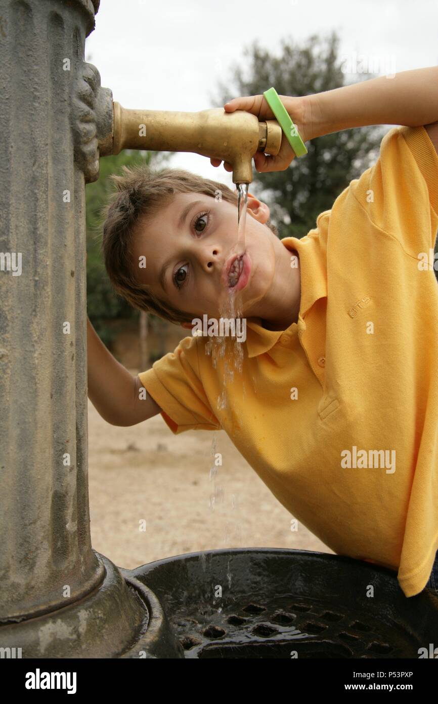 Niño de seis años bebiendo agua en una fuente. Stock Photo