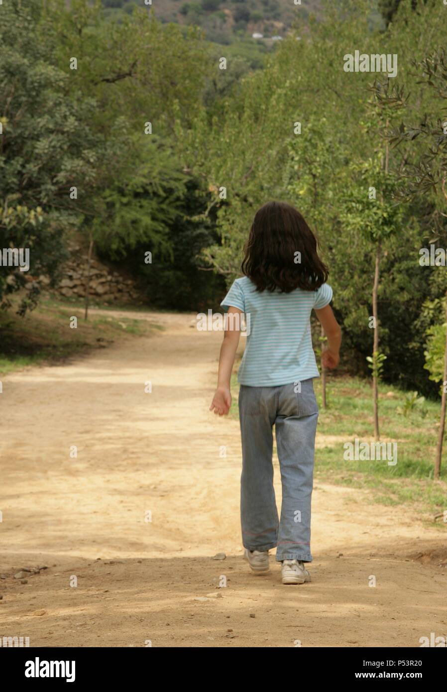 Niña de siete años, de espaldas, andando por un camino. Stock Photo