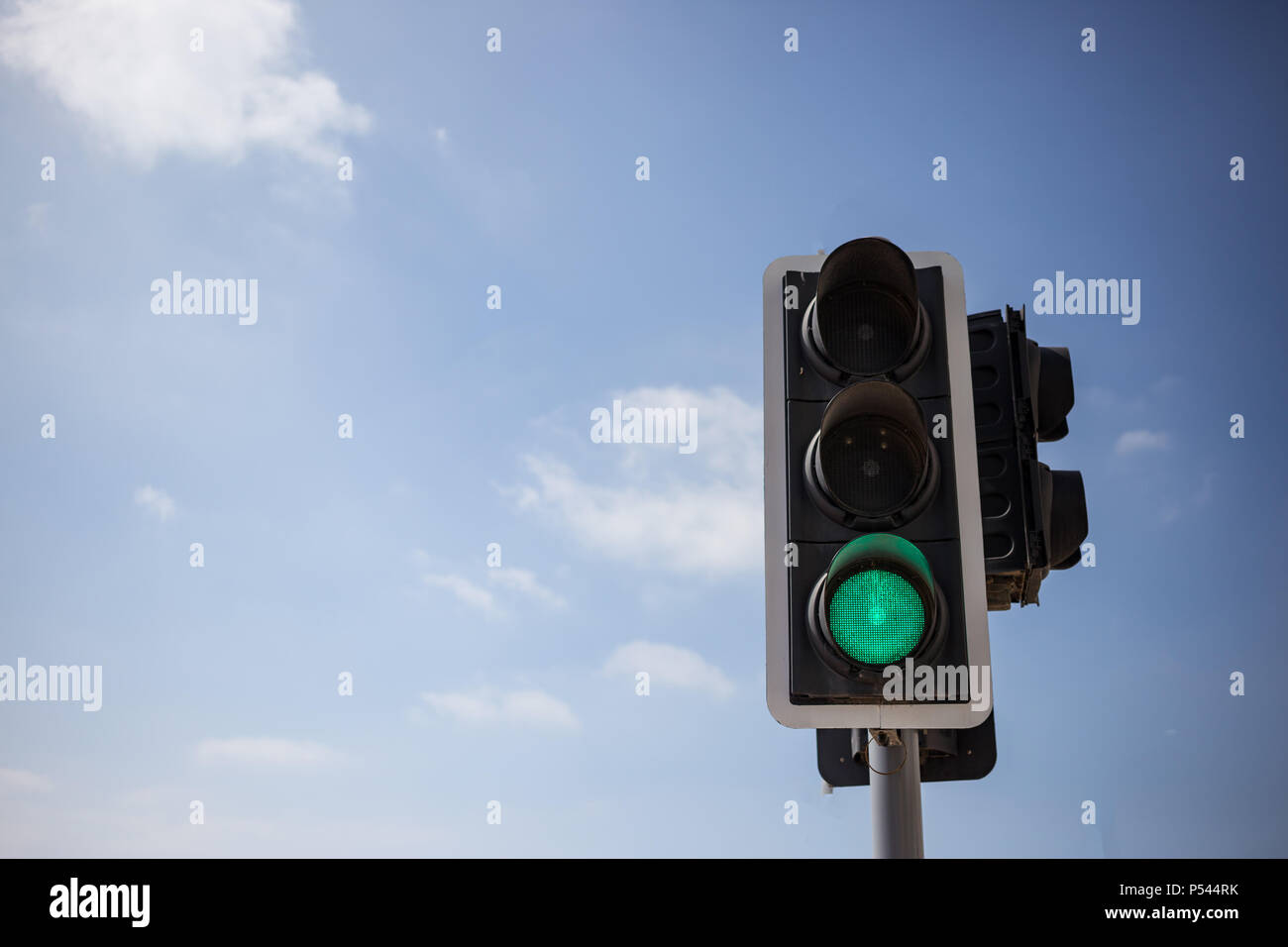 Green traffic light. Signal that it is safe to go on the way. Blue sky with few clouds background. Close up under view, space for text. Stock Photo