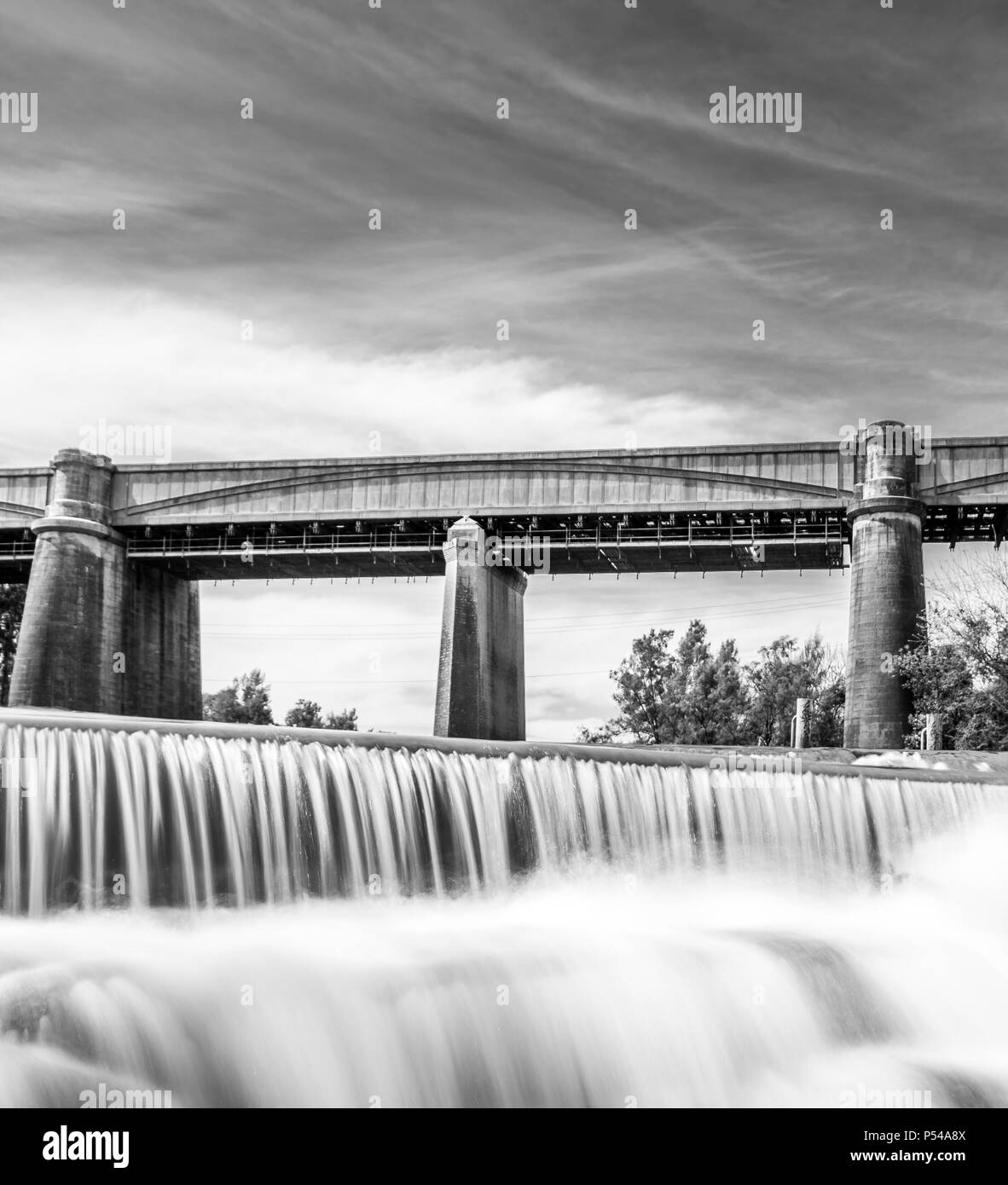 Black and White Neutral Density shot of a Waterfall with a train bridge in the background Stock Photo