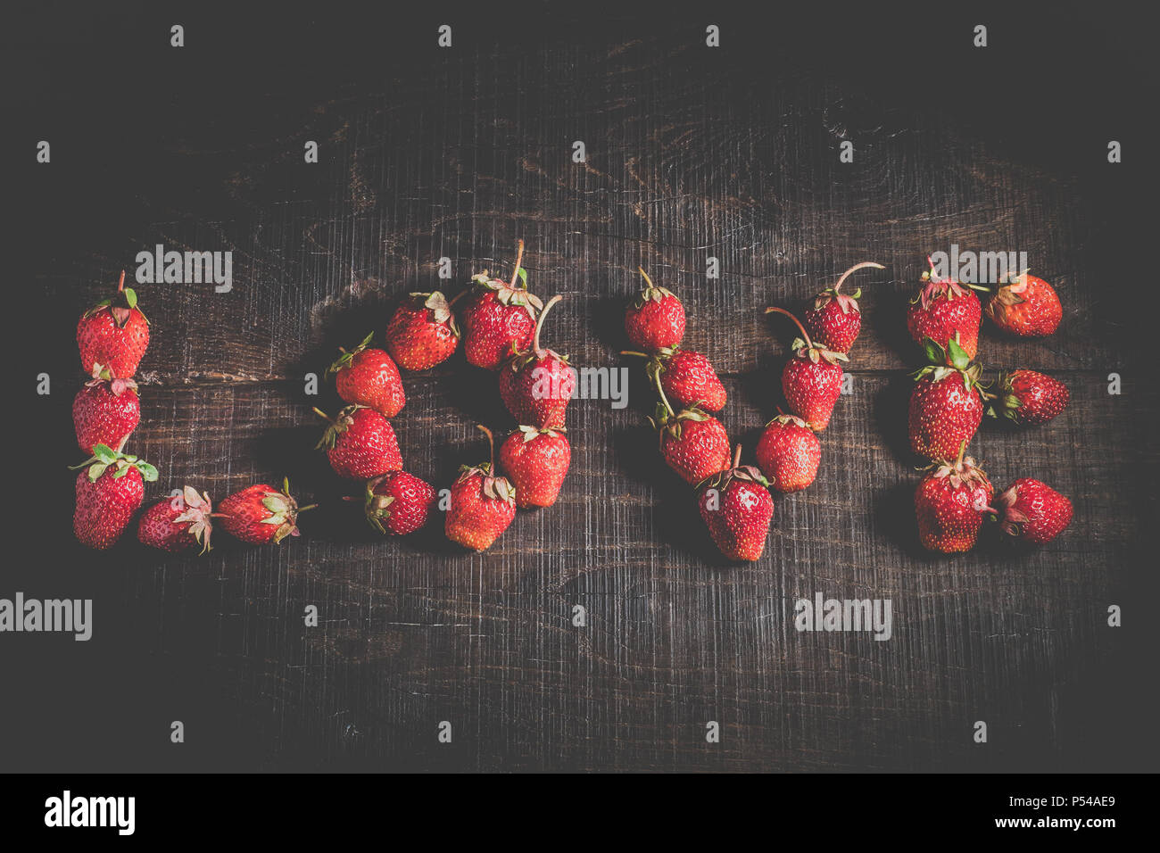 Strawberry in the form of the word love. The inscription is love. Ripe strawberry fruit. Strawberries on a wooden background. Healthy food. Stock Photo