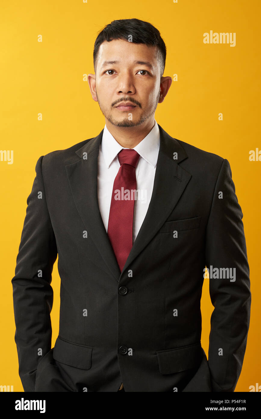 Portrait of young asian businessman with hands in pocket isolated on yellow background Stock Photo