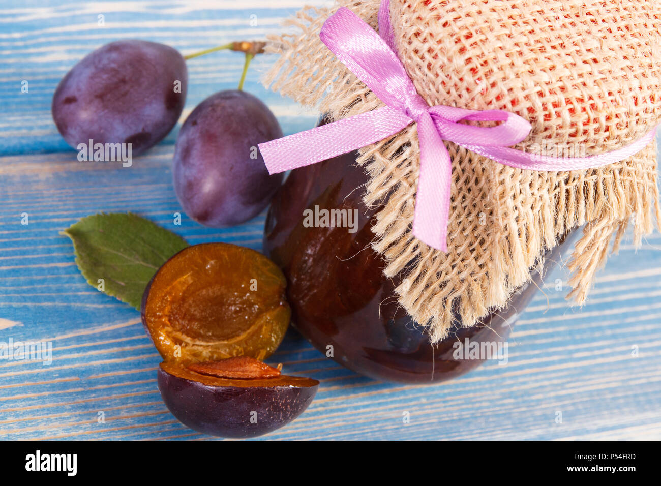 Fresh plum jam or marmalade in glass jar and ripe fruits on blue boards, concept of healthy sweet dessert Stock Photo
