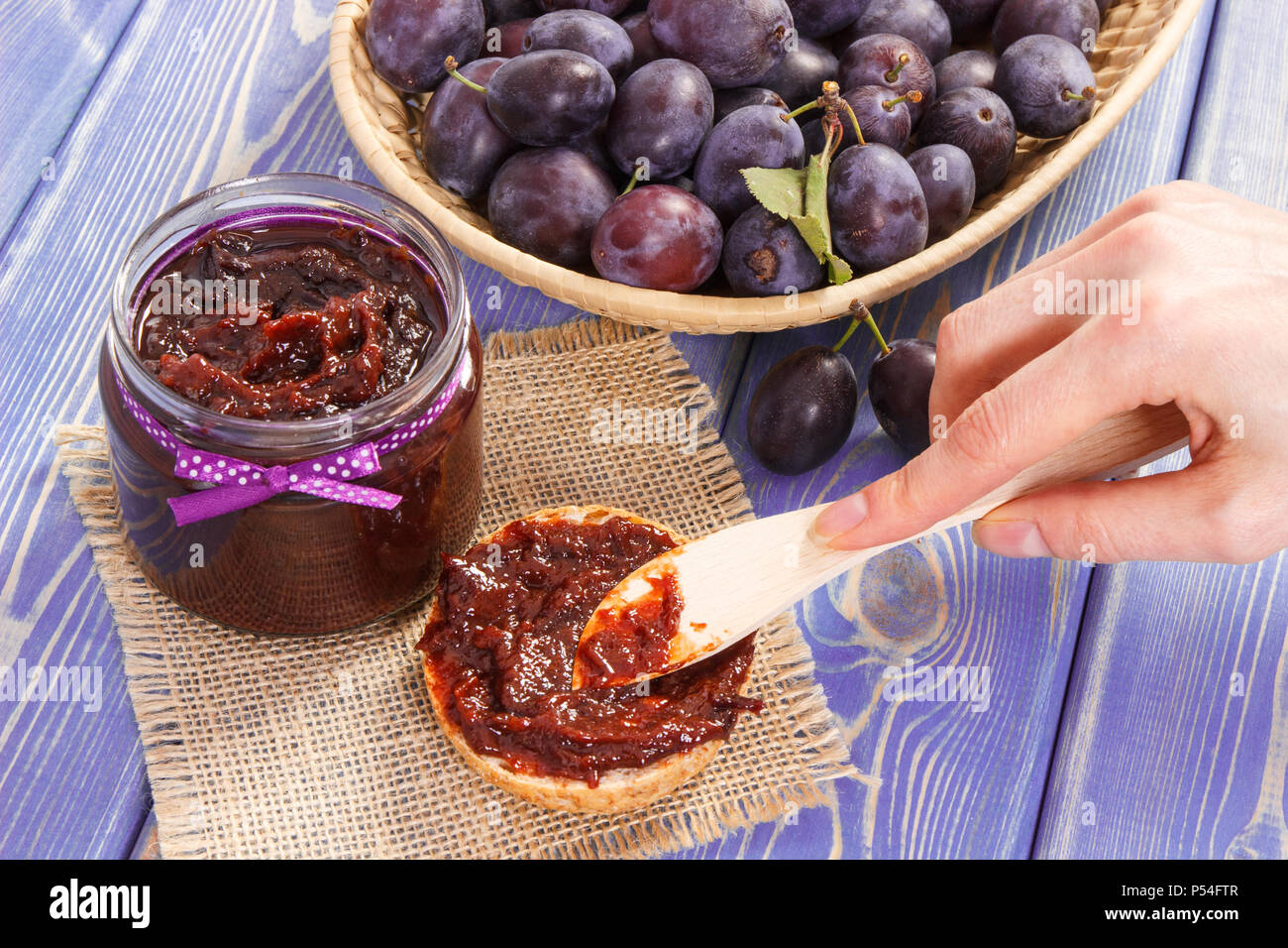 Hand with knife preparing fresh sandwiches with plum marmalade or jam, concept of healthy sweet snack, breakfast or dessert Stock Photo
