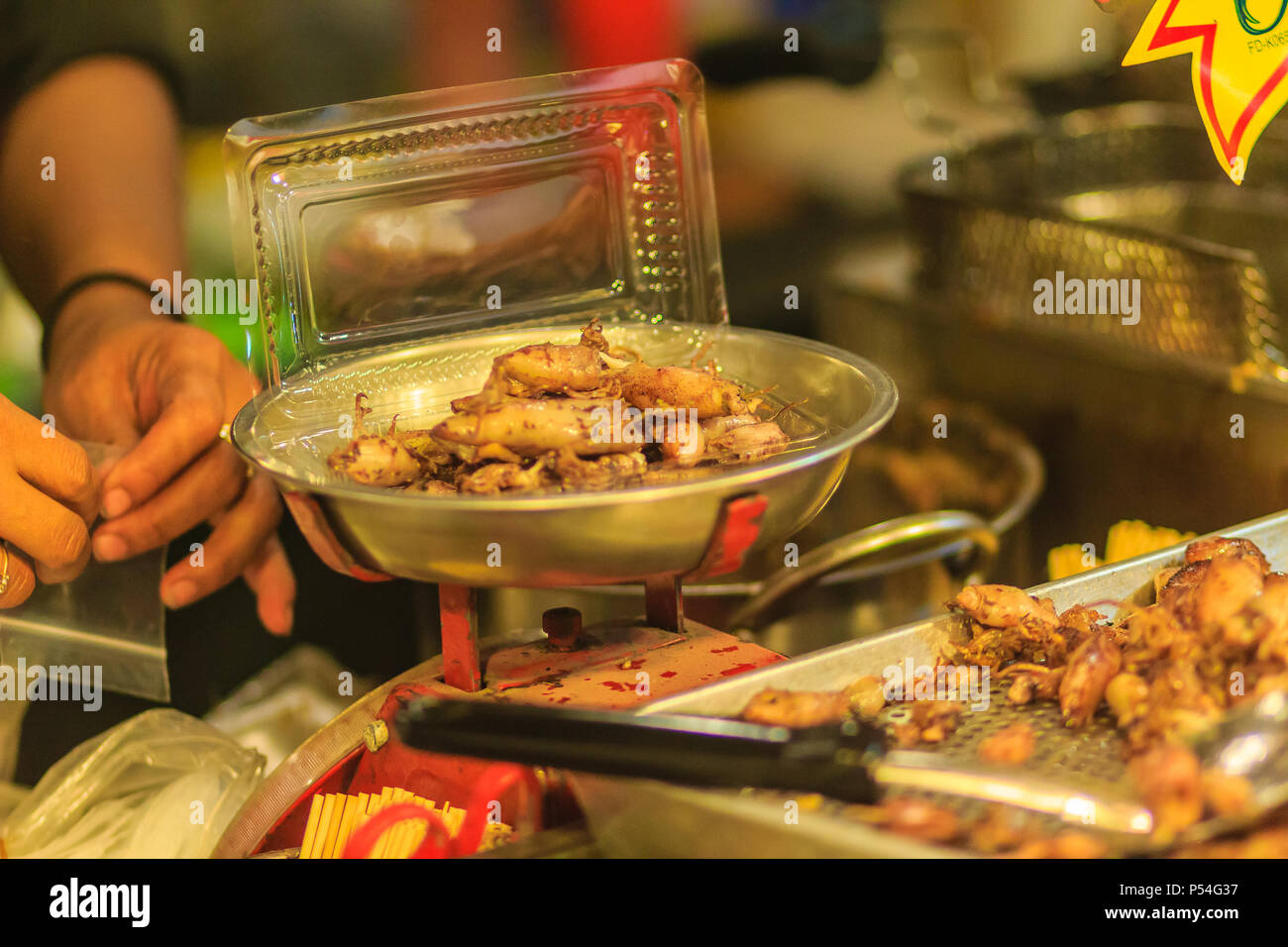 Vendor is selling fried baby squid with garlic in night market at Bangkok, Thailand. Stock Photo