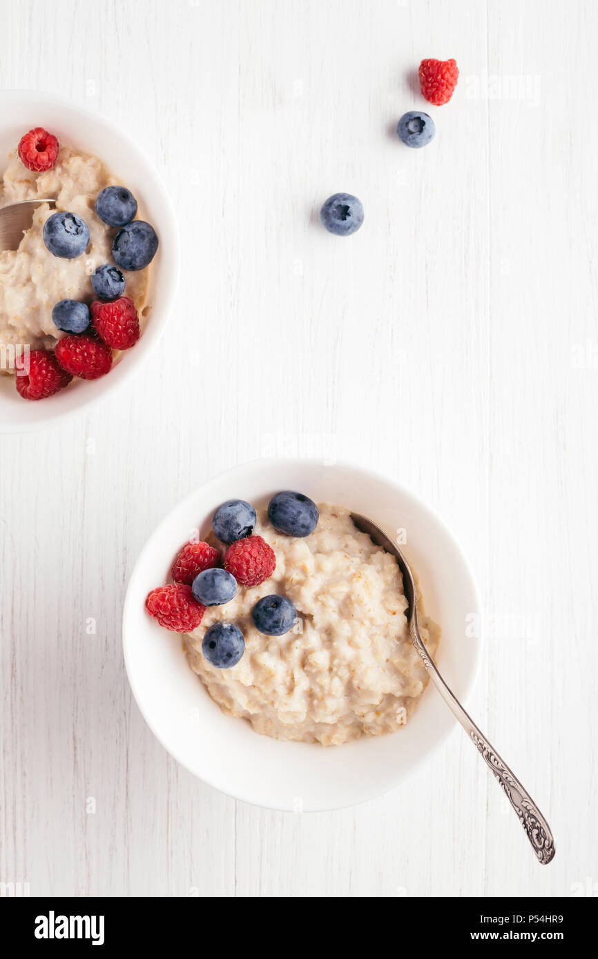 A bowl of oatmeal porridge with blueberries and raspberries on white wooden table. Top view. Stock Photo