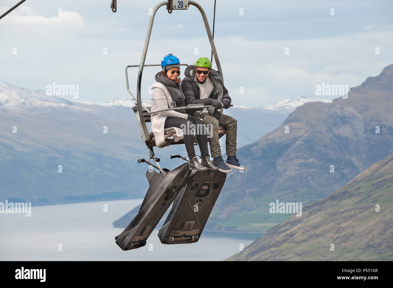 Queenstown, NZ – April 15, 2018: Fun riders with their carts on a cable chair lift going up the hill top for a luge ride with views of Lake and hills. Stock Photo