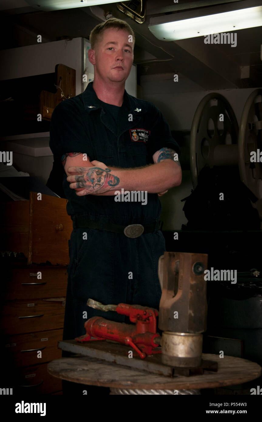 MANAMA, Bahrain (May 9, 2017) Mineman 2nd Class Tyler Smith, a native of Munford, Ala. and assigned to the Avenger-class mine countermeasure ship USS Devastator (MCM 6), poses for a photo in front of a nicopress, which makes mechanical or electro-mechanical connections to secure sweep lines. On April 23, Smith deployed to the Avenger-class mine countermeasure ship USS Dextrous (MCM 13) and repaired the ship’s swage, a thick metal clasp that secures the ship’s sweep wire and withstands up to 18,000 pounds of pressure. Stock Photo