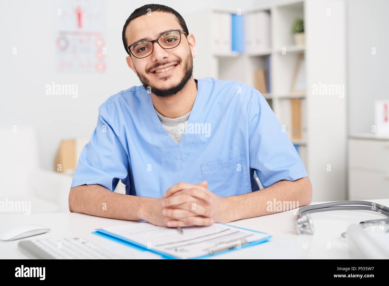 Smiling Middle-Eastern Doctor Posing at Desk Stock Photo