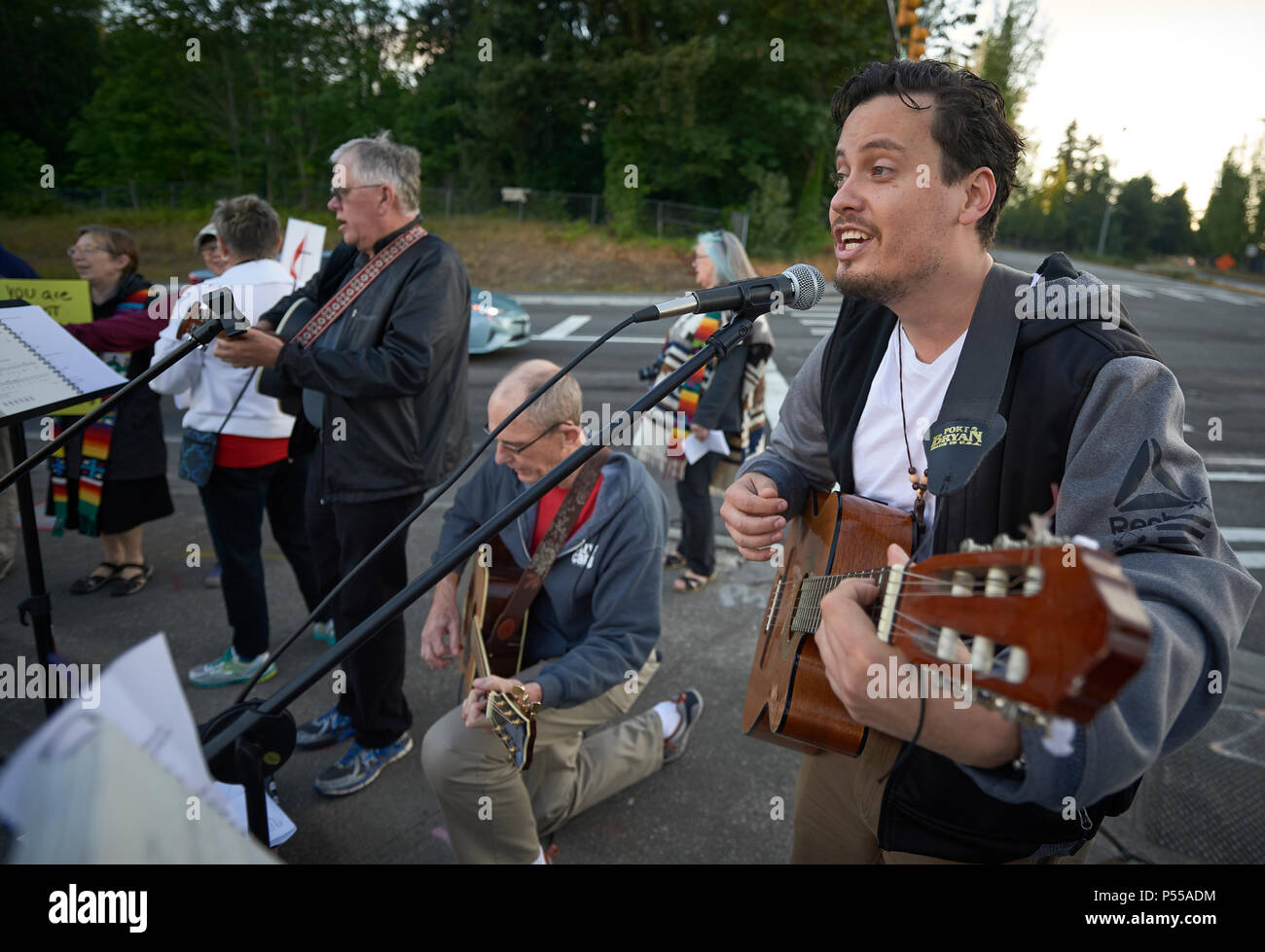 Seatac, Washington, USA. 24 June, 2018.  Joel Rodriguez leads singing outside the Federal Detention Center in Seatac, Washington, early June 24 during a prayer vigil in support of immigrant parents inside the prison who've been separated from their children. Behind him is David Reinholz. The vigil was sponsored by the United Methodist Church.  Credit: Paul Jeffrey/Alamy Live News Stock Photo